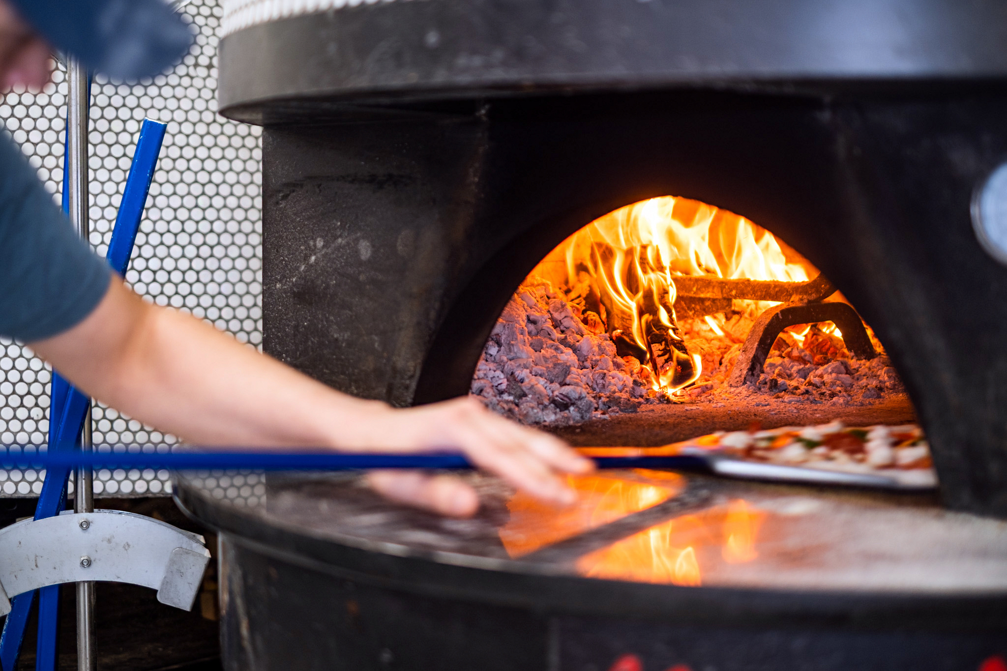 A chef wades into a fiery oven with a pizza paddle.