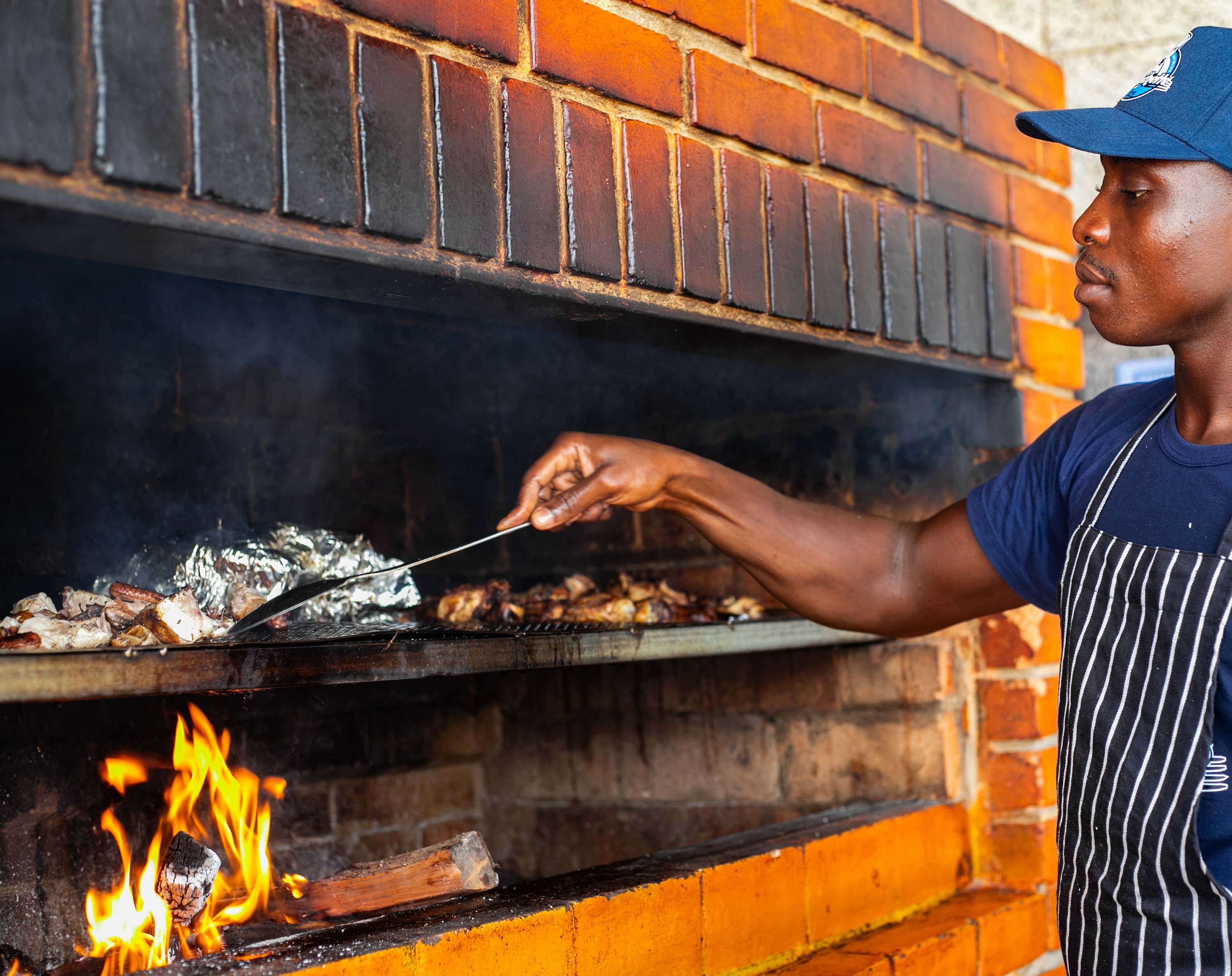 A chef grills items in foil in a brick-lined wood oven.