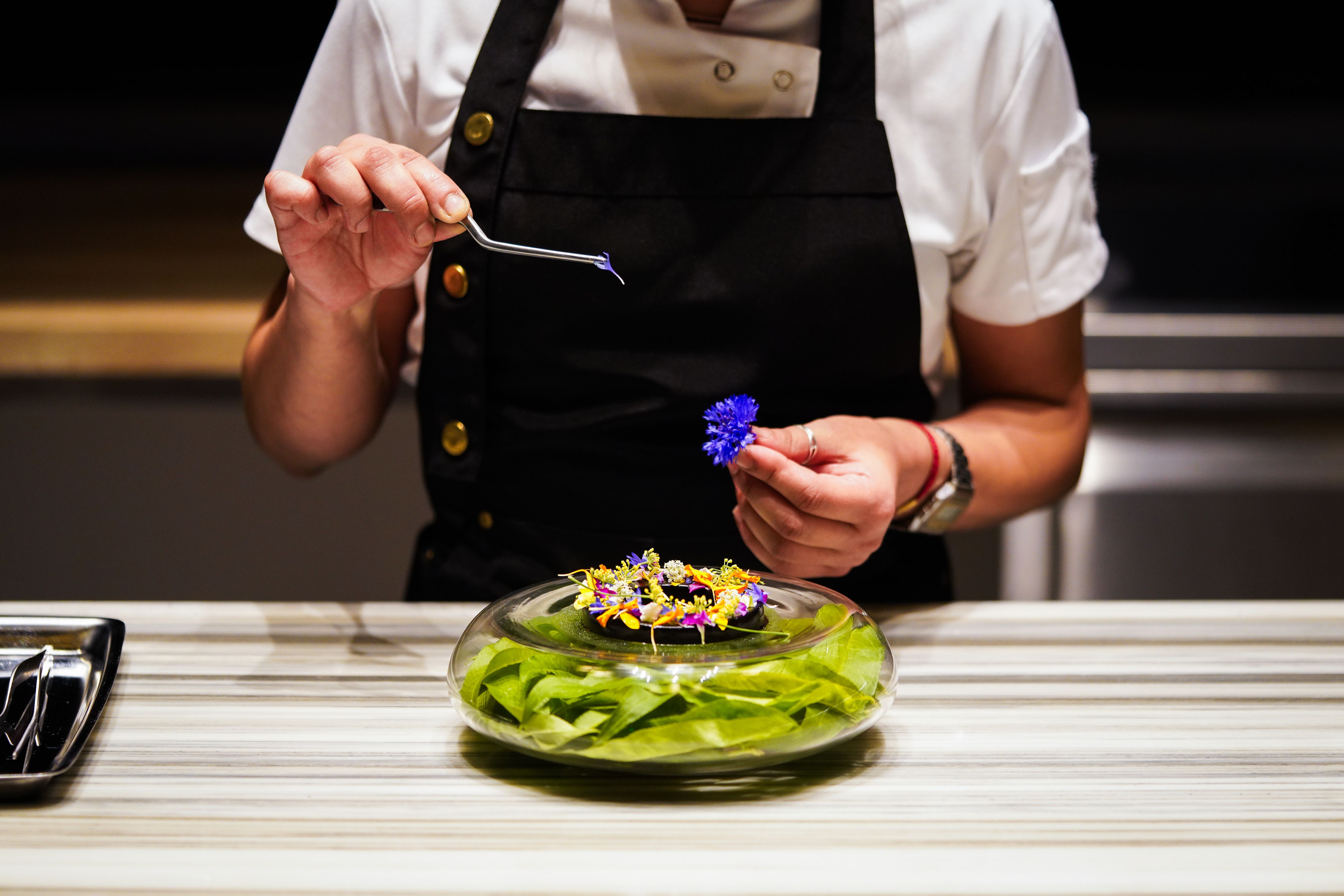 A person uses twitters to pluck petals from a flower to attach to a dish.