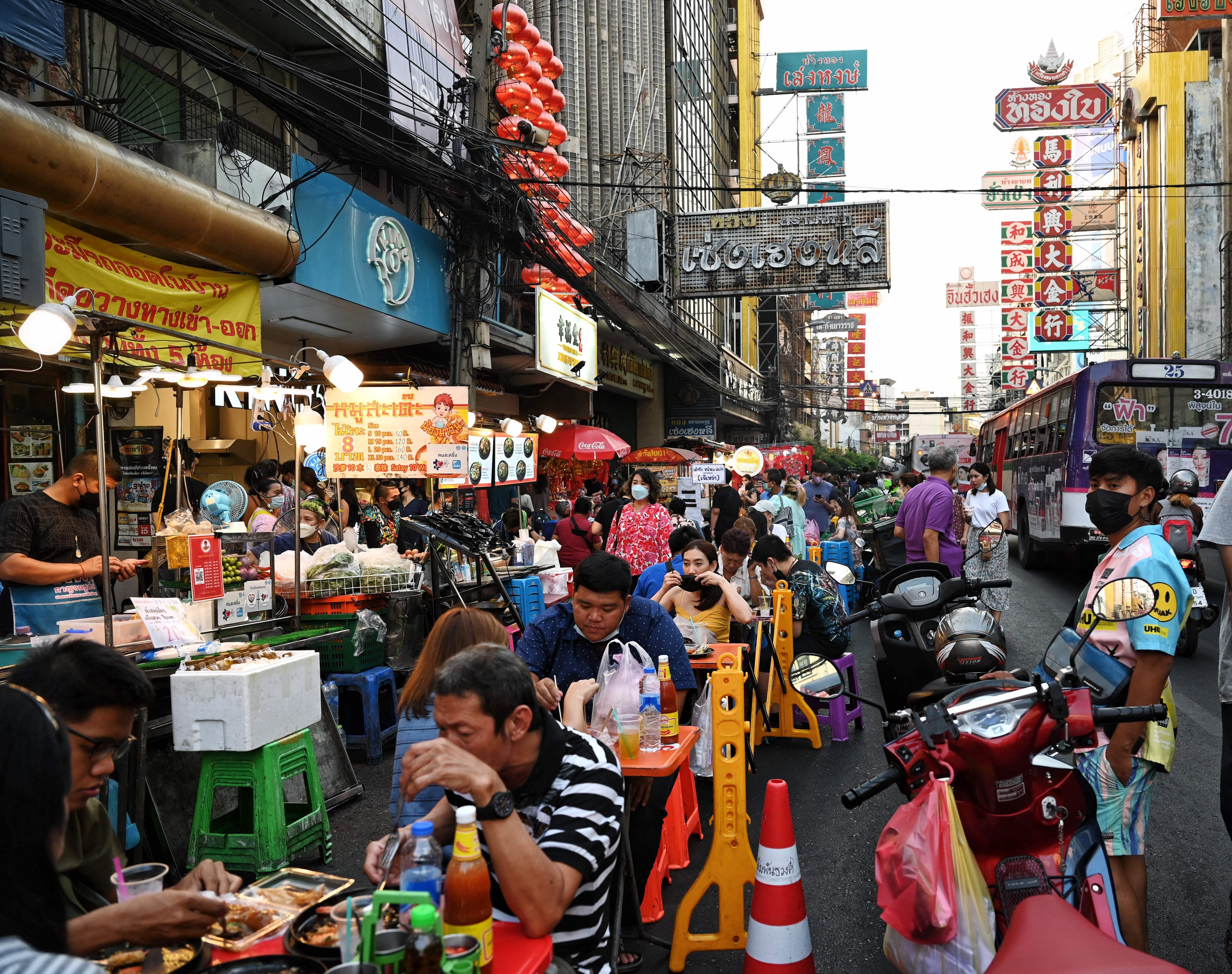 Diners enjoy meals at plastic tables on a busy street. 
