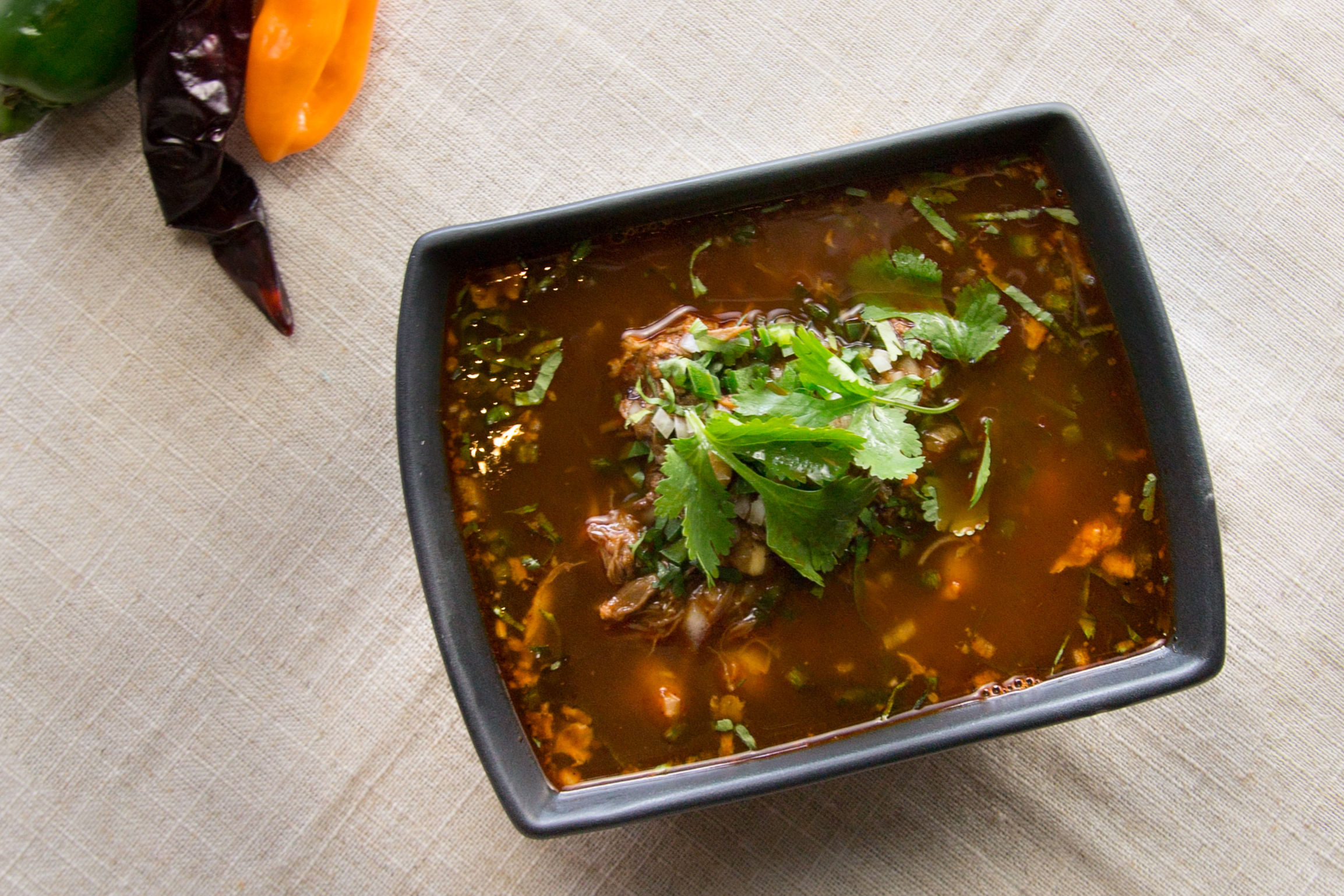 A black square-ish bowl filled with a red-toned soup topped with cilantro.