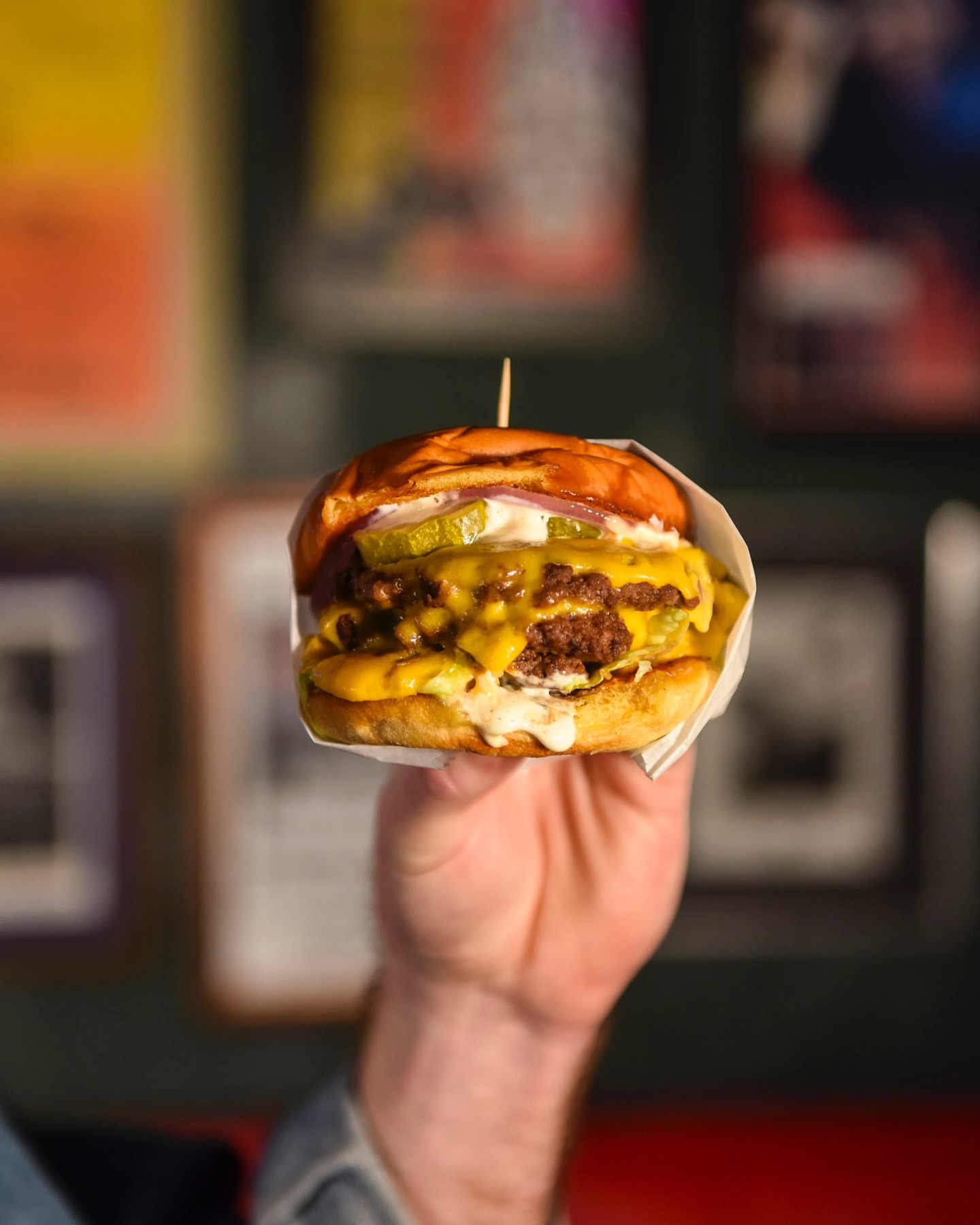 A white hand holding up a double cheeseburger.