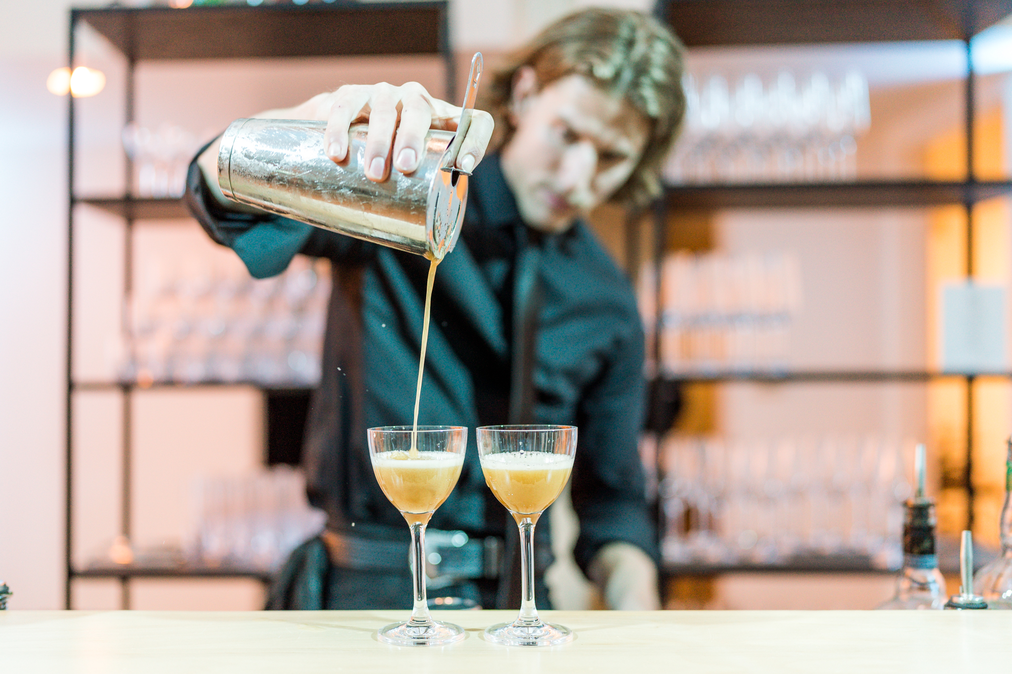 A bartender pours cocktails into glasses.
